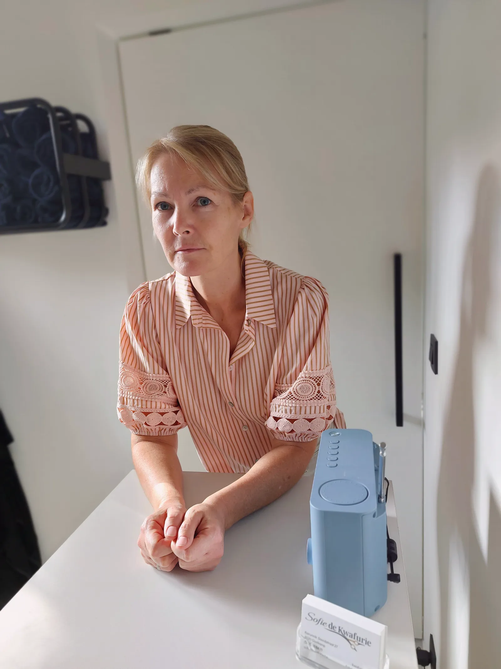 Sofie aan de toog in het salon, met haar visitekaartjes naast zich