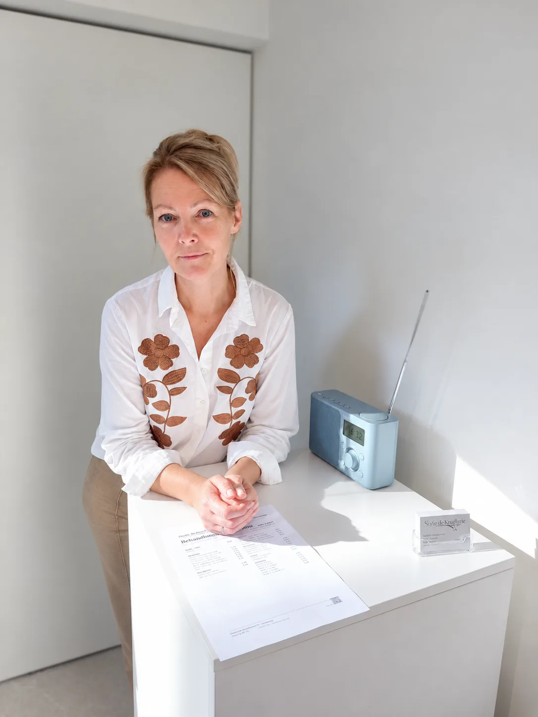 Sofie aan de toog in het salon, met een radio en haar visitekaartjes naast zich
